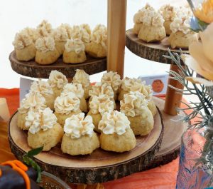 Mini banana maple bundt cakes topped with swirls of brown sugar buttercream and golden sprinkles, displayed on a rustic wood-slab tiered stand. Part of a cozy-chic wedding dessert table at Danville Bed & Breakfast in Geneva, Florida. A handcrafted fall dessert by The Cookie Jar Orlando for weddings, showers, and special events.