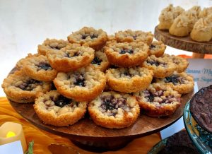 A stacked display of blueberry baby pies with a golden shortbread crust and streusel topping, styled on a wooden dessert stand. Part of a rustic boho dessert table at a wedding at Danville Bed & Breakfast in Geneva, Florida. Baked by The Cookie Jar Orlando.