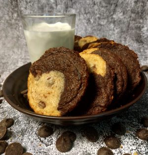 Brookie cookies featuring a half-brownie, half-chocolate chip cookie swirl, arranged in a dark bowl with a glass of milk and chocolate chips scattered nearby. A decadent hybrid treat by The Cookie Jar Orlando, ideal for weddings, parties, and corporate dessert trays.