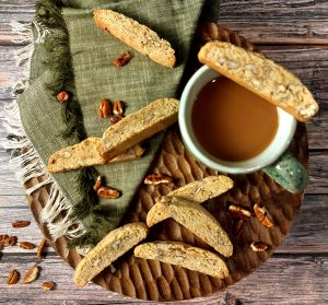 Golden butter pecan biscotti cookies with chopped nuts, styled with a rustic coffee mug on a wooden tray. A warm and elegant treat for fall weddings, holiday parties, or corporate gift boxes in Central Florida. Baked by The Cookie Jar Orlando.
