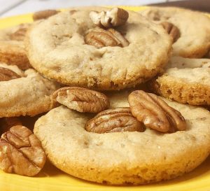 Golden brown butter pecan cookies topped with whole toasted pecans, arranged on a vibrant yellow tray. A rich, nutty cookie from The Cookie Jar Orlando, ideal for wedding dessert tables, holiday trays, corporate gifting, and celebration favors.