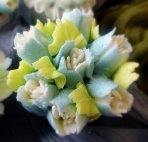 Detailed close-up of a pastel blue and green buttercream floral cupcake with white petal centers, designed for elegant events like weddings, bridal showers, baby showers, and Mother's Day.