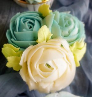 Cupcake decorated with three buttercream roses in white and soft teal, accented with pale green leaves, perfect for weddings, bridal showers, baby showers, and Mother’s Day.