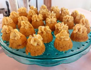 Mini butterscotch bundt cakes topped with golden buttercream swirls, arranged on a vintage teal glass stand at a rustic wedding dessert table. Served at The Wedding Barn in Oviedo, Florida by The Cookie Jar Orlando — perfect for weddings, baby showers, sweet sixteens, and fall celebrations.
