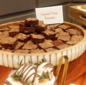 Fudgy chocolate caramel pecan brownies arranged on a round wooden tray, part of a warm and elegant wedding dessert table at The Covenant Church in Palm Coast, Florida. Created by The Cookie Jar Orlando for weddings, showers, and celebrations.