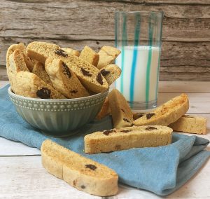 A bowl of handmade chocolate chip biscotti cookies with crisp golden edges, styled with a glass of milk on a rustic blue cloth. A versatile treat for weddings, parties, or corporate gifting in Central Florida by The Cookie Jar Orlando.