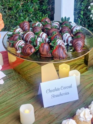 A gold pedestal tray filled with milk and white chocolate covered strawberries, featured on an enchanted forest-themed wedding dessert table at Cypress Grove in Orlando.