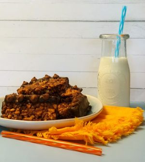 Thick chocolate peanut butter Rice Krispy treats stacked on a plate, paired with a vintage-style milk bottle and bright orange napkin—perfect for parties, sweet treats, and dessert tables in Central Florida.