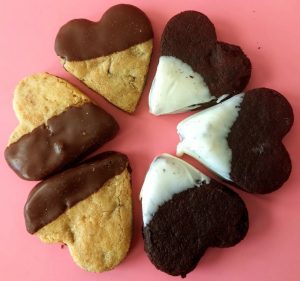 Assorted heart-shaped cookies — chocolate chip dipped in dark chocolate, and brownie dipped in white chocolate — arranged on a pink background. A festive treat for weddings, bridal showers, birthday parties, sweet sixteen events, and quinceañeras in Central Florida. Created by The Cookie Jar Orlando.
