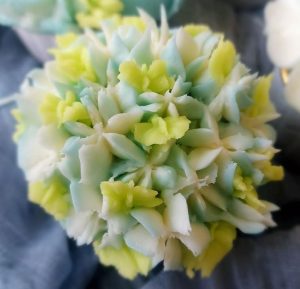 Cupcake topped with blue, green, and ivory buttercream piped in a hydrangea flower pattern, ideal for weddings, bridal showers, baby showers, and spring-themed events.