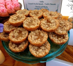 Mini lemon baby pies with a French shortbread crust and brown sugar streusel topping, arranged on a teal glass dessert stand. Part of a vibrant dessert display at a wedding at Danville Bed & Breakfast in Geneva, Florida. Made by The Cookie Jar Orlando for weddings and special events.