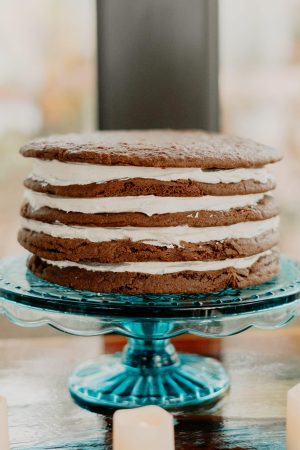 Rustic-style Oreo-inspired chocolate cookie cake layered with white buttercream, served on a vintage blue glass stand. A unique dessert centerpiece for weddings, bridal showers, or baby showers at Casani Estates in Central Florida. Created by The Cookie Jar Orlando.