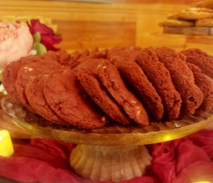 Red velvet white chocolate chip cookies arranged on a glass stand at rustic Orlando wedding dessert table.