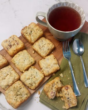 Mini savory scones made with herbs, cheese, and bacon served on a wooden board with a cup of tea—perfect for brunch parties, weddings, and corporate events in Orlando, St. Augustine, Daytona, and surrounding Central Florida areas.