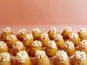Mini strawberry bundt cakes topped with pale blush buttercream rosettes, displayed on a soft pink background. A romantic, hand-crafted dessert from The Cookie Jar Orlando, perfect for weddings, baby showers, sweet sixteens, and modern dessert tables.