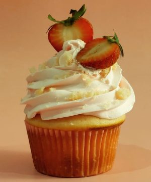 Vanilla cupcake with a swirl of light pink strawberry buttercream, cake crumb topping, and fresh strawberry halves. Ideal for bridal showers, baby showers, Mother's Day, and summer celebrations.