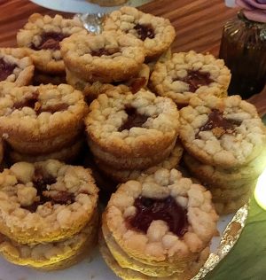 Stacks of sugar plum baby pies with buttery French shortbread crust and brown sugar streusel topping, displayed on a white dessert stand at a Christmas party at Northwest Square in DeLand, Florida. A festive holiday dessert from The Cookie Jar Orlando, perfect for weddings, showers, and events.