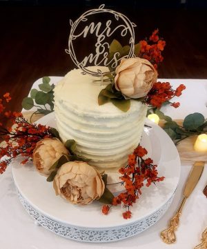 Small sweetheart buttercream wedding cake with ridged frosting design, topped with a “Mr & Mrs” wooden topper and decorated with soft peach peonies and orange floral accents. Styled for a wedding at Covenant Church in Palm Coast, Florida by The Cookie Jar Orlando.