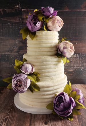 Three-tier textured buttercream wedding cake with purple flowers for weddings in Orlando, Daytona, and St. Augustine areas.