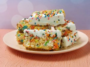 Fruity Rice Krispy treats dipped in white chocolate and topped with colorful rainbow sprinkles, stacked on a pink plate—perfect for birthdays, kids’ parties, school events, sweet sixteens, and celebrations across Central Florida.